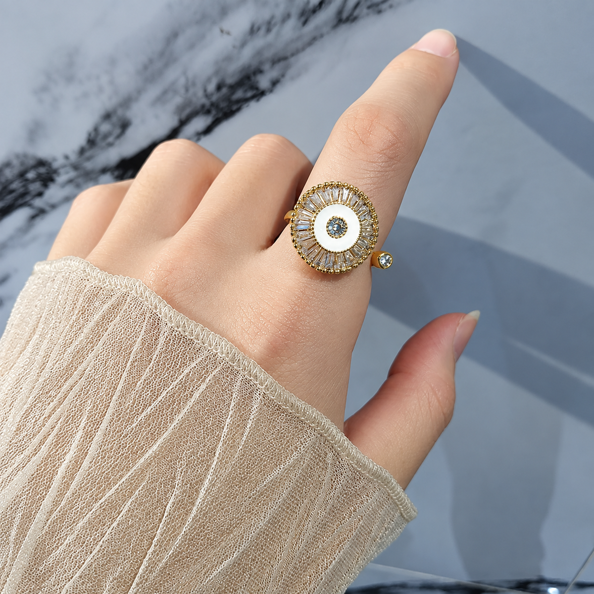 Bague anti-stress rotative Épicycle dorée, médaillon émaillé blanc couronné de pierres baguette, portée au doigt