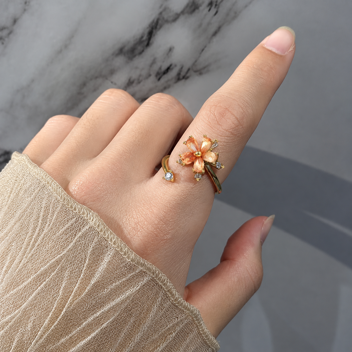 Bague anti-stress rotative Fleur Cosmique dorée, fleur aux pétales en pierres pêche et pierres taille baguette, portée au doigt